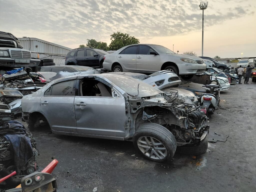 Silver scrap sedan among vehicles at a Scrap Car Adda collection yard in the UAE